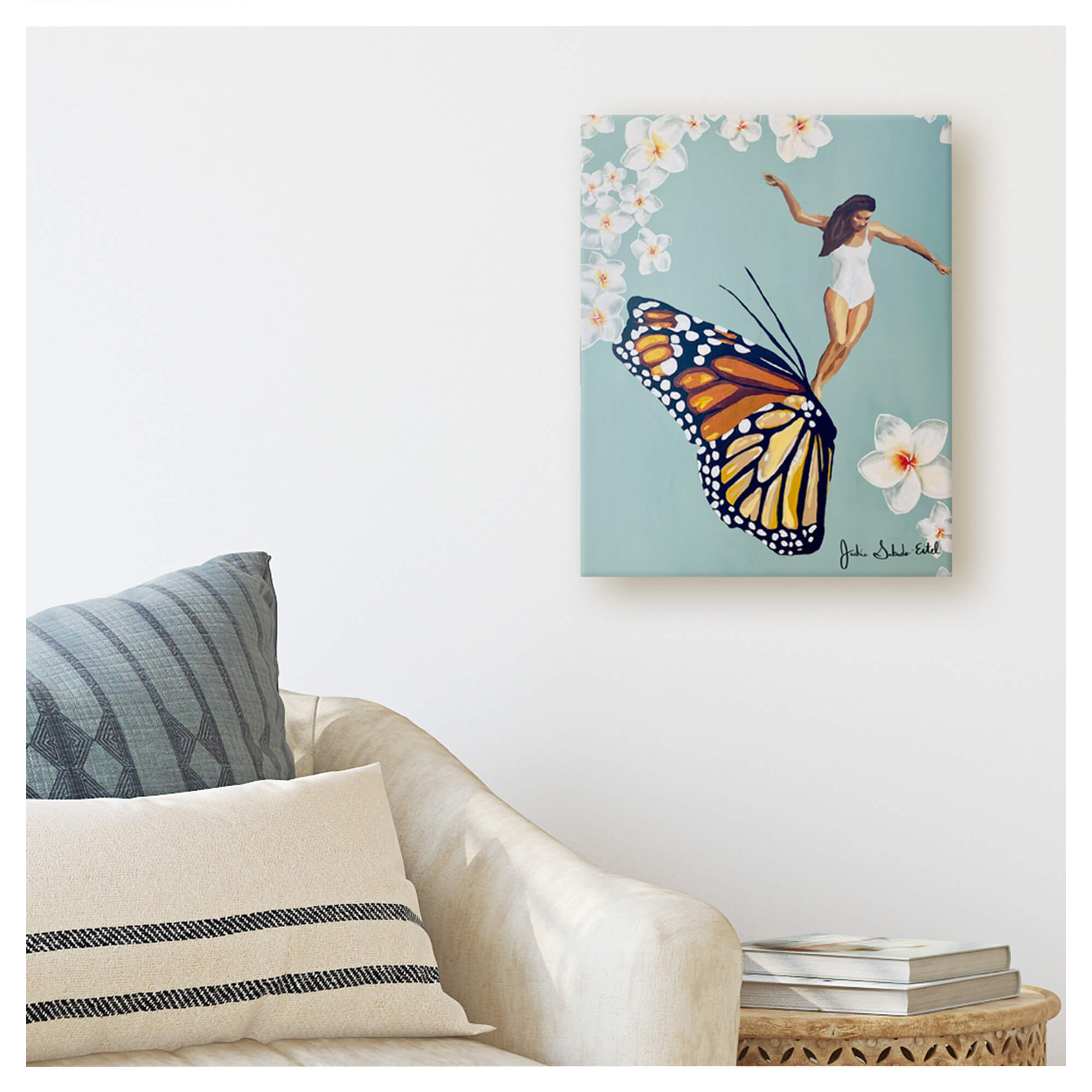 A canvas giclée print featuring a woman riding a butterfly framed by plumeria flowers on a pastel teal-hued background by Hawaii artist Jackie Eitel