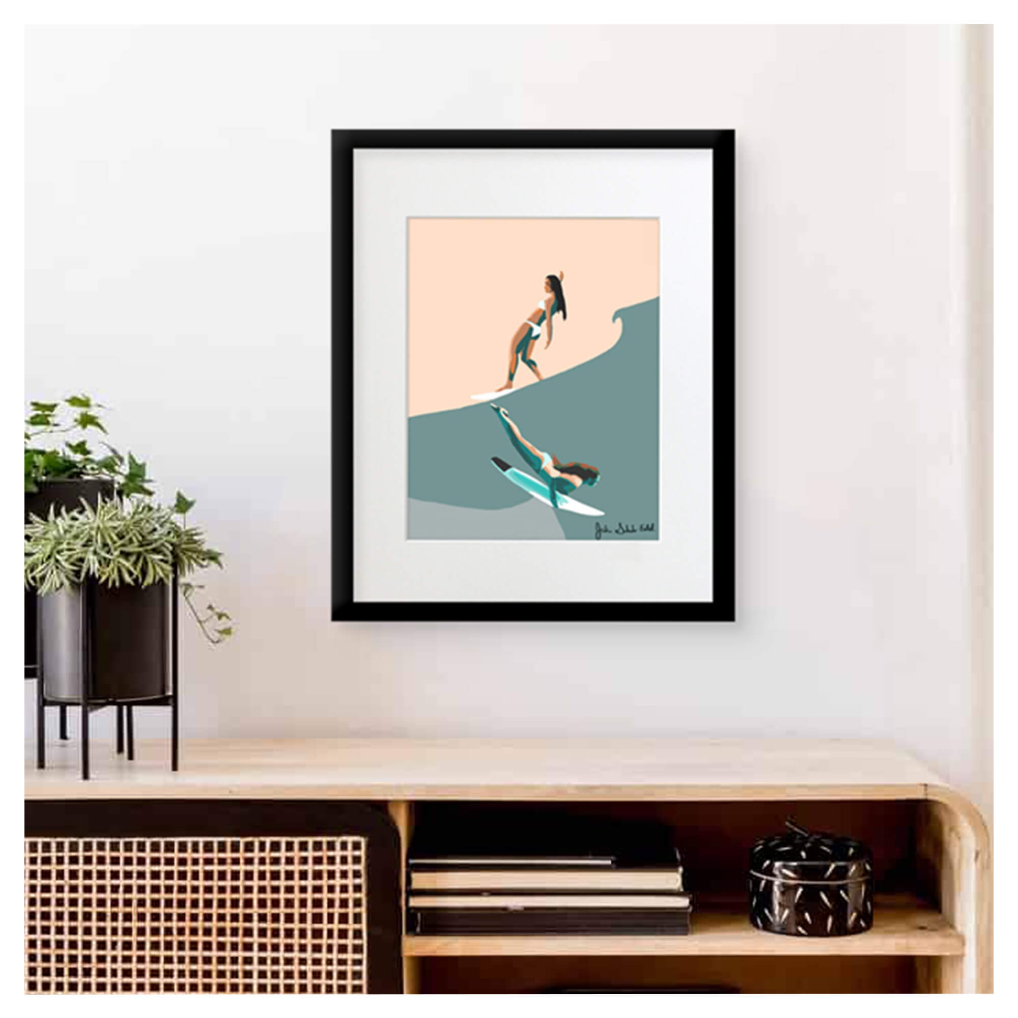 A framed matted art print featuring two female surfers, one riding the waves and the other just right beneath by Hawaii artist Jackie Eitel