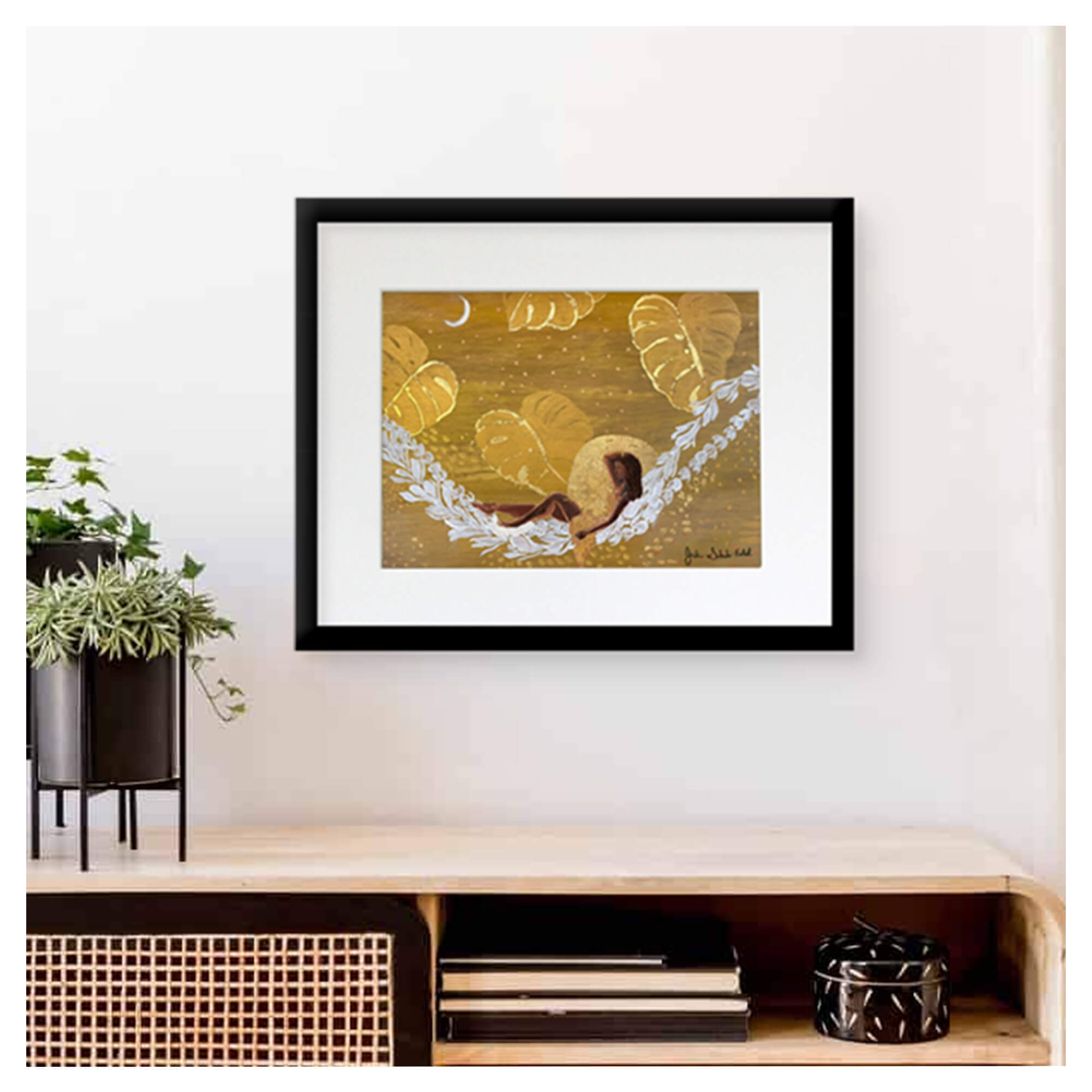 A framed matted art print featuring a woman relaxing on a lei hammock with monstera leaves backdrop and some gold touchups by Hawaii artist Jackie Eitel